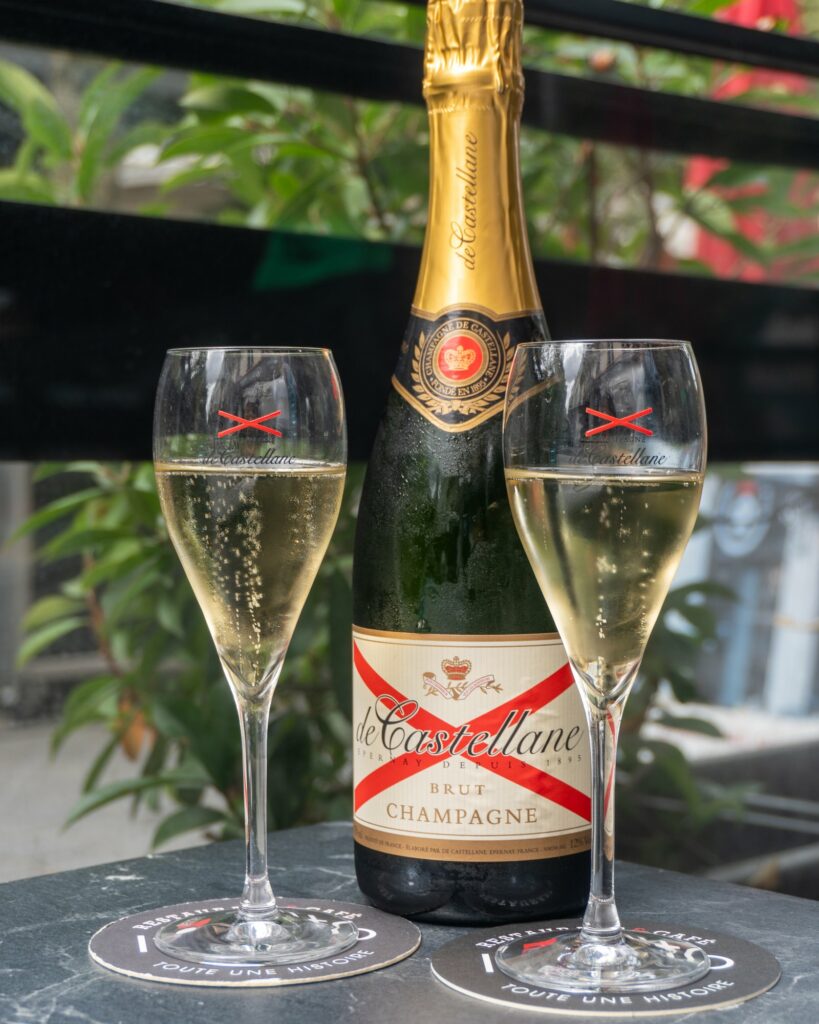 Bouteille de Champagne De Castellane entre deux flûtes, en terrasse